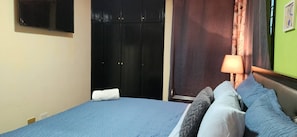 A bedroom with a bed, a wall-mounted TV, a wardrobe, and a lamp. - Spacious and Comfortable 3-bedroom 2 Bathroom in Santo Domingo Este (Santo Domingo Este)