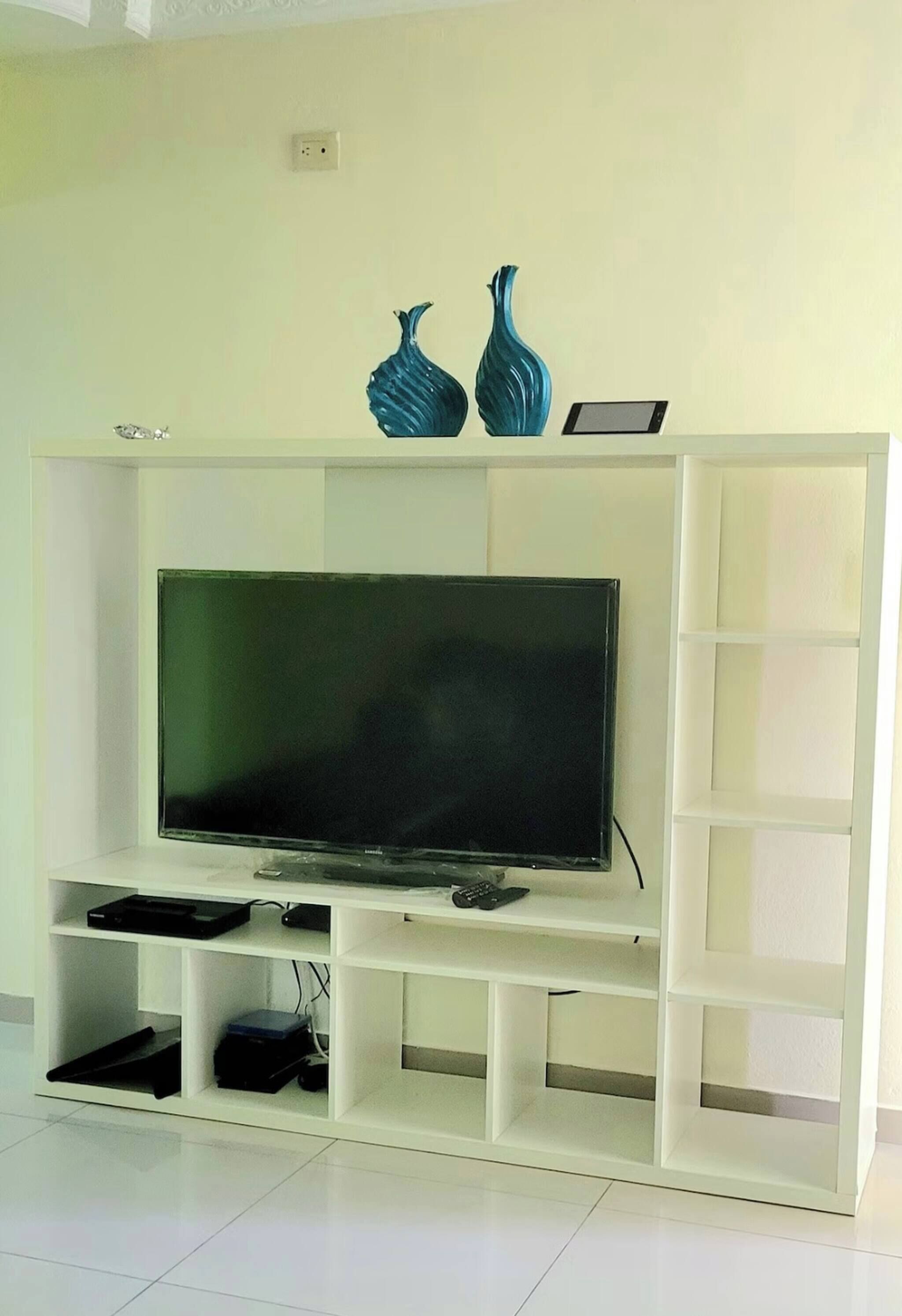 A white entertainment unit with a flat-screen TV, two decorative vases, and a tablet.