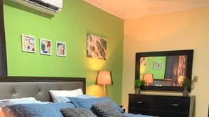 Quarto de hotel com uma cama grande, televisão de tela plana, escrivaninha com abajur e obras de arte nas paredes.