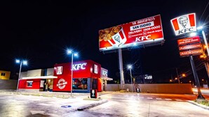 Restaurante KFC à noite com iluminação exterior vibrante e um grande painel publicitário.