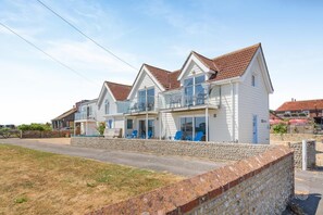 A row of white houses with red roofs, each with a balcony and blue chairs. - 1 Bed in Selsey (oc-s36029) (Selsey)