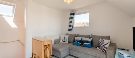 A cozy room with a grey sofa, a wooden side table, a small cabinet, and a ceiling light fixture.