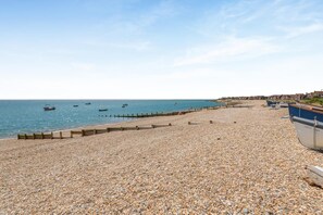 A pebbled beach with boats, a wooden fence, and buildings in the background. - 1 Bed in Selsey (oc-s36029) (Selsey)