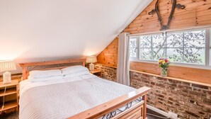 Een slaapkamer met een houten bed, een stenen muur, een raam met uitzicht en een lamp op een nachtkastje.