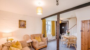 Een gezellige woonkamer met een bank, stoelen, een eettafel en een trap naar een andere kamer.