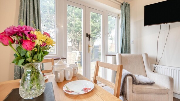 A dining area with a table set for four, a vase of flowers, and a chair. - 2 Bed in Hunston (oc-g36324) (Hunston)