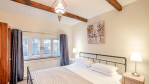 A bedroom with a bed, bedside lamps, a window with curtains, a radiator, and a painting on the wall. - 2 Bed in Hunston (oc-g36324) (Hunston)