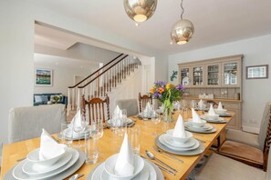 A dining area with a wooden table set for a meal, a staircase in the background, and a kitchen with cabinets. - 6 Bed in Hadlow Down (oc-g36329) (Hadlow Down)