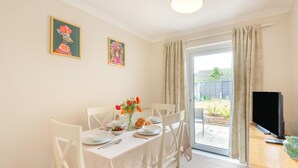 A dining area with a table set for four, a vase of flowers, and a television on a stand. - 2 Bed in Cromer (oc-c36333) (Cromer)