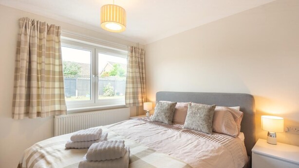 A bedroom with a bed, two bedside lamps, a window with curtains, and a radiator. - 2 Bed in Cromer (oc-c36333) (Cromer)