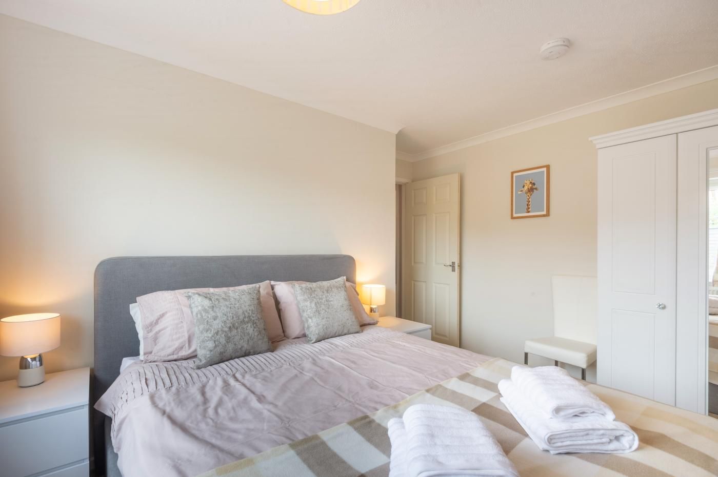 A bedroom with a bed, bedside lamps, a wardrobe, and a framed picture on the wall.
