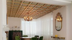 A dining area with a patterned ceiling, a chandelier, a round table with chairs, and a decorative mirror.