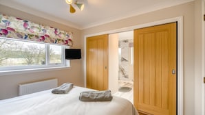 Una camera da letto con un letto, una televisione, una finestra e una porta in legno che dà su un bagno.