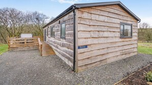 Una baita in legno con tetto spiovente, un portico e una strada di accesso sterrata.