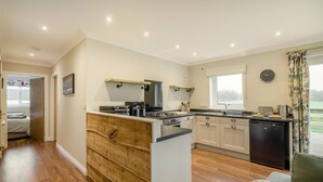 A modern kitchen with a central island, wooden cabinetry, and a dining area with a view. - 2 Bed in Ochiltree (oc-w37517) (Ochiltree)