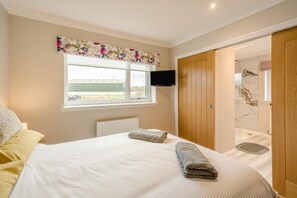 A bedroom with a bed, a window, a television, and a wooden door leading to a bathroom.