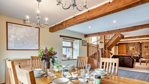 A dining area with a wooden table set for four, surrounded by wooden chairs. A chandelier hangs from the ceiling, and a map is displayed on the wall. - 2 Bed in Brecon (oc-44182) (Llanfihangel Nant Bran)