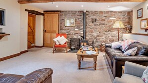 A cozy living room with a stone wall, a fireplace, a leather sofa, a wooden chair, and a coffee table. - 2 Bed in Brecon (oc-44182) (Llanfihangel Nant Bran)