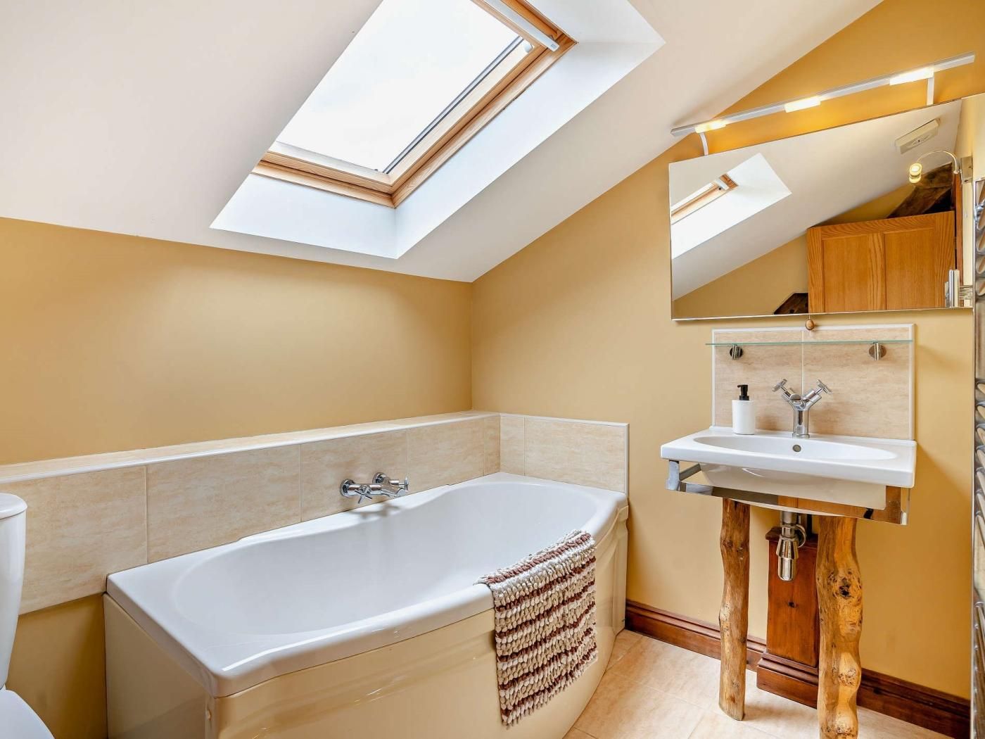 Een moderne badkamer met dakraam, een vrijstaand bad, een wastafelmeubel met spiegel en een toilet.