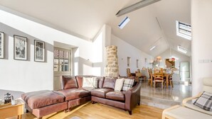 Un salon spacieux avec un canapé d’angle en cuir, un coin repas doté de meubles en bois et un mur d’accent en pierre.