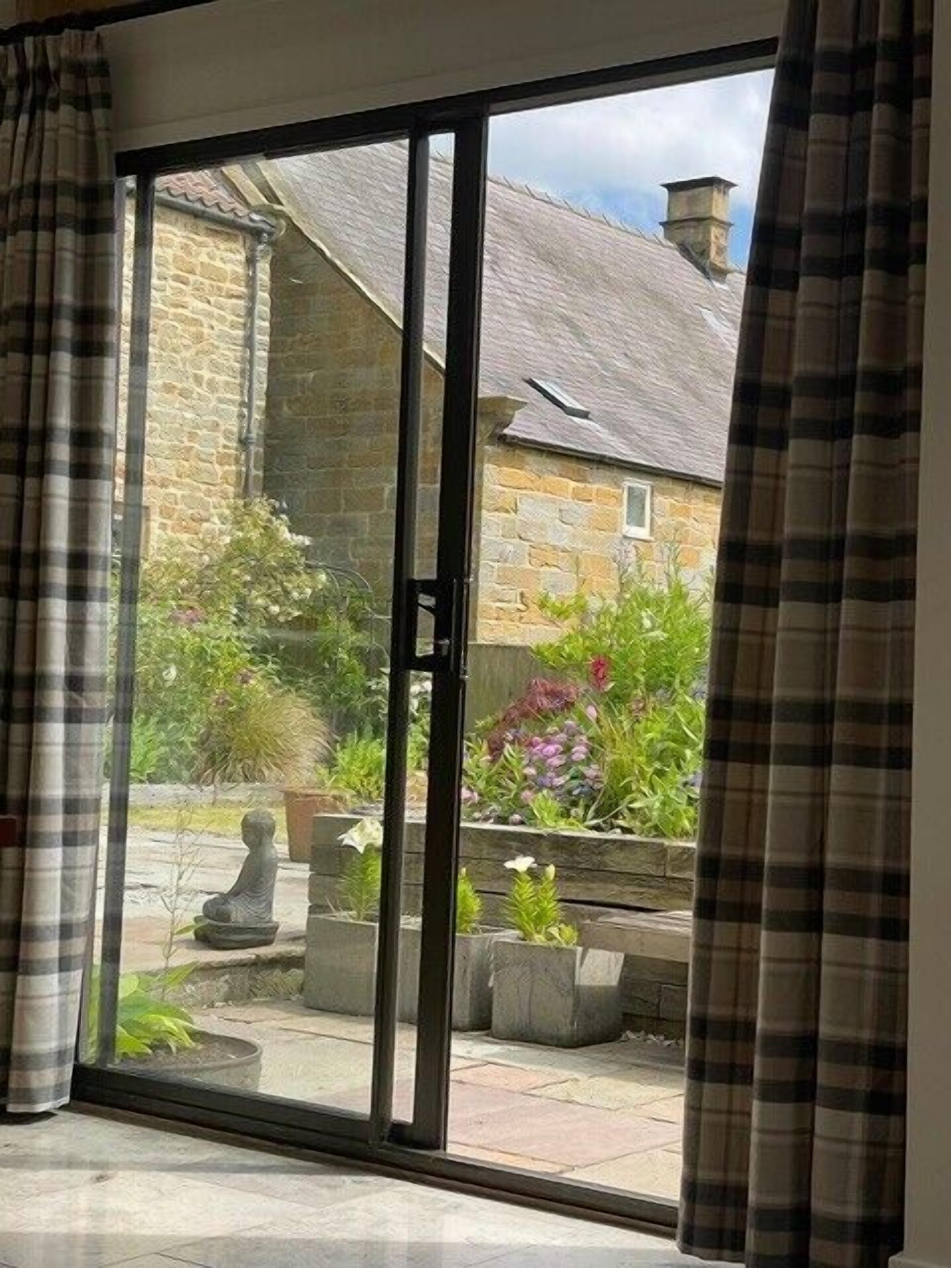 A room with a sliding glass door leading to a garden with stone planters and a stone wall.