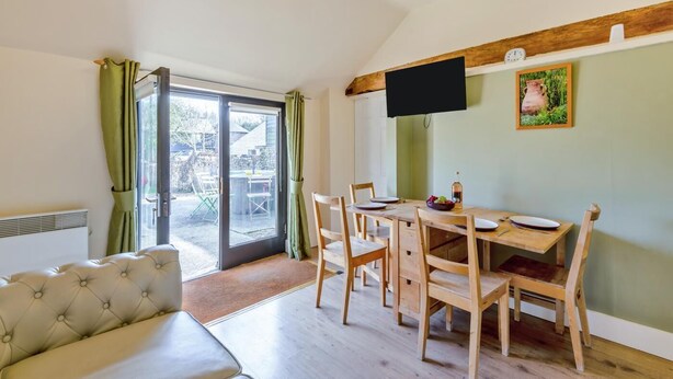 Een kamer met een eettafel, stoelen, een bank, een televisie en een schuifdeur naar een buitenruimte.