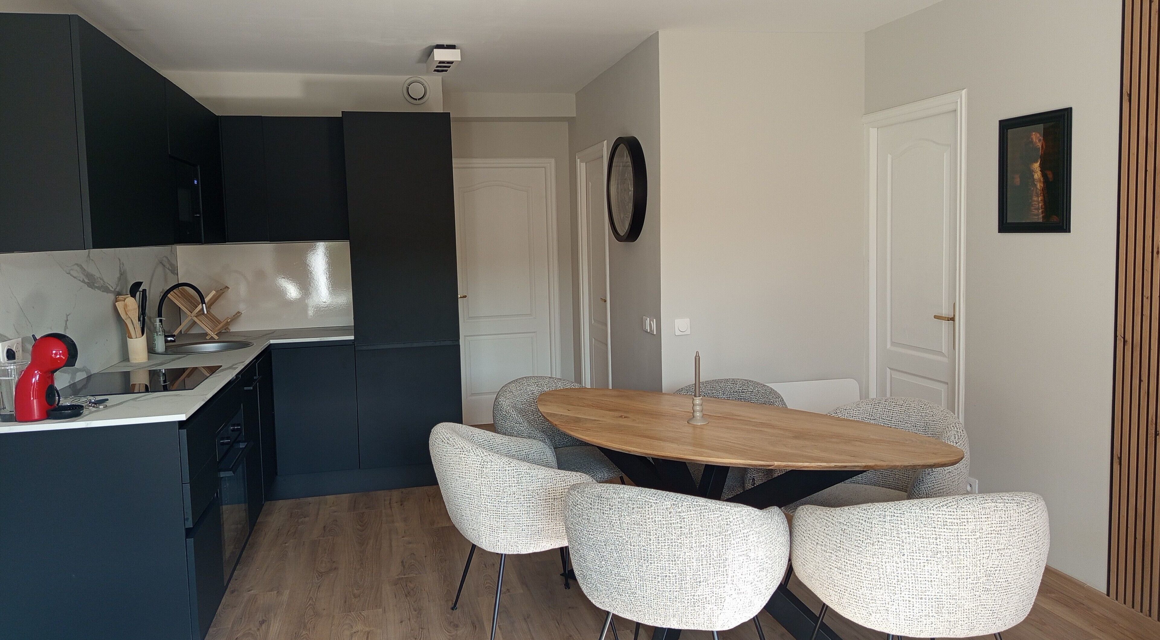 Une cuisine moderne avec des meubles de rangement de couleur sombre, une table à manger en bois et quatre chaises à motifs.