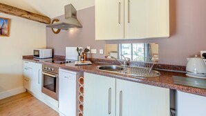 Una cucina compatta con mobili bianchi, un lavello in acciaio inox, un forno a microonde, un forno e una macchina da caffè.