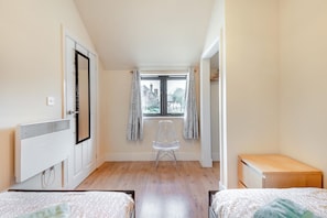 Ein Schlafzimmer mit zwei Betten, einem Heizkörper, einem Fenster mit Vorhängen und einem Stuhl.