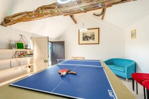 Ein Zimmer mit einem Tischtennis-Tisch, einem blauen Sofa, einem roten Sessel, einem Bücherregal und einem gerahmten Bild an der Wand.