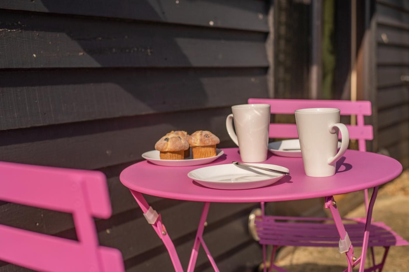 Un tavolo rosa all'aperto con un piatto di muffin, una tazza bianca e un cucchiaio.