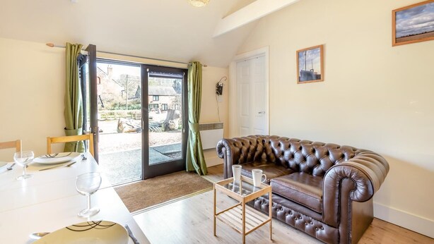 Ein Wohnzimmer mit Ledersofa, einem Esstisch mit Stühlen, einer Glastür, die nach draußen führt, und einer Hängelampe.