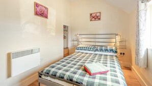Ein Schlafzimmer mit Bett, Nachttisch, Wandregal und einem Fenster mit Vorhängen.