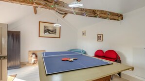 Ein Zimmer mit einem Tischtennis-Tisch, roten Stühlen, einem gerahmten Bild an der Wand und einem Holzbalken an der Decke.