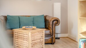 Ein Wohnzimmer mit einer Ledersofa, Kissen in Türkis, einem Holznachttisch und einem Bücherregal.