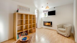 Ein Wohnzimmer mit Bücherregal, Kamin, Wand-Fernseher und einem bequemen Sessel.