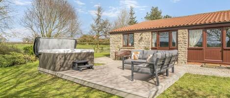 A patio with outdoor furniture, a barbecue grill, and a stone building with a tiled roof.