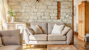 A living room with a stone wall, a sofa, a wooden cabinet, and a window. - 2 Bed in Great Edstone (oc-t36332) (Great Edstone)