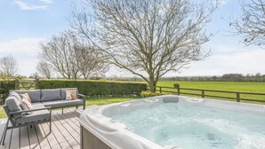 A hot tub on a wooden deck with a gray sofa and cushions, surrounded by a hedge and a tree. - 2 Bed in Great Edstone (oc-t36332) (Great Edstone)