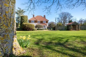A large house with a red-tiled roof, surrounded by a well-maintained lawn and a wooden fence. - 5 Bed in Holme Next The Sea (oc-2265) (Holme-next-the-Sea)