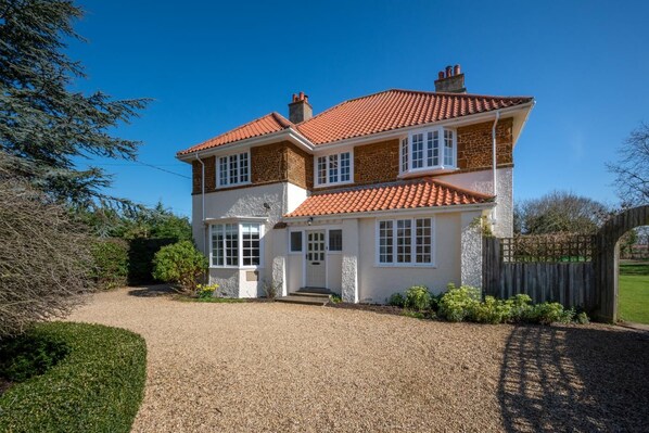 A two-story house with a red-tiled roof, white exterior walls, and a gravel driveway. - 5 Bed in Holme Next The Sea (oc-2265) (Holme-next-the-Sea)
