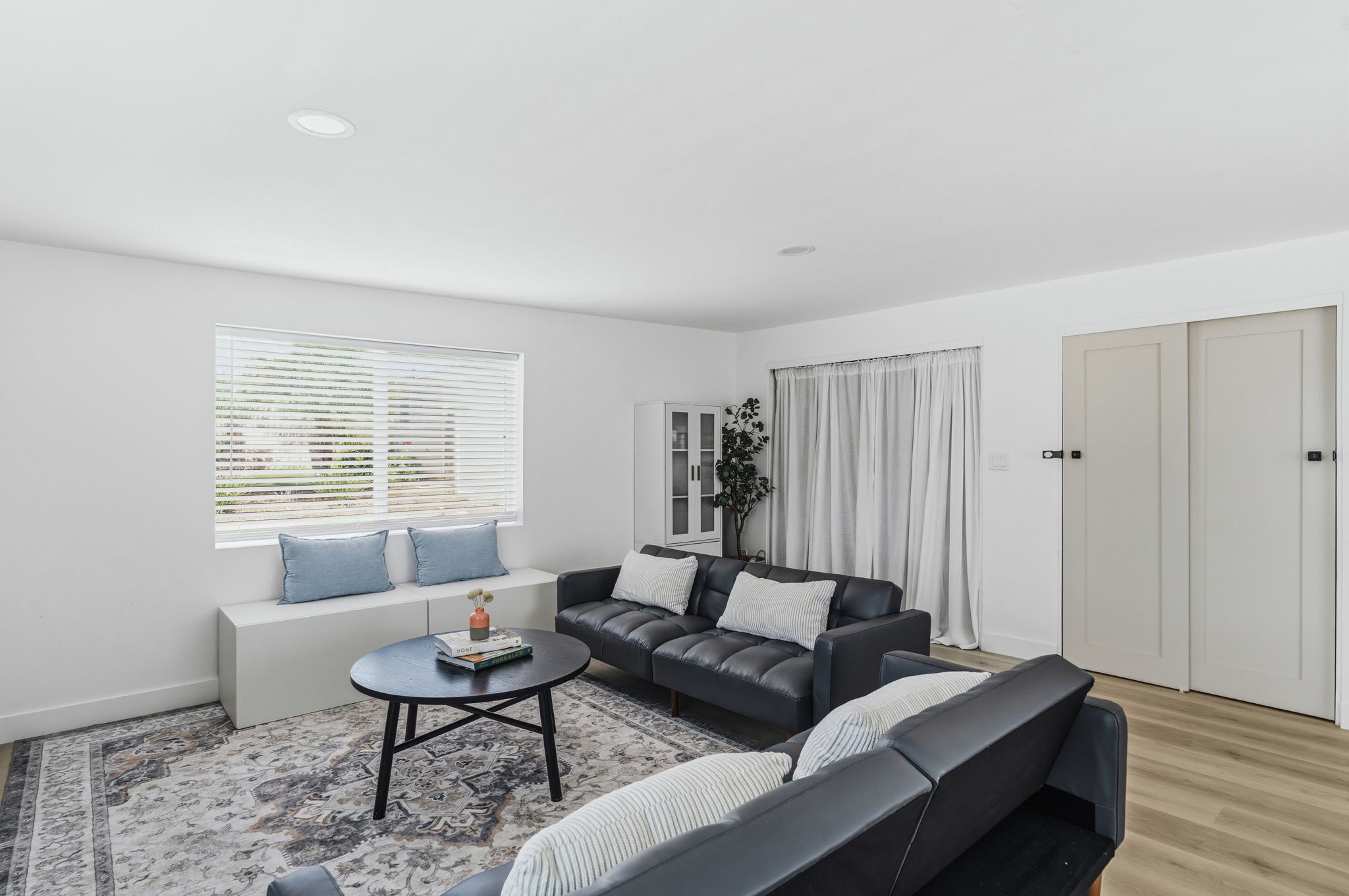 A modern living room with a sofa, a coffee table, and a window with blinds.
