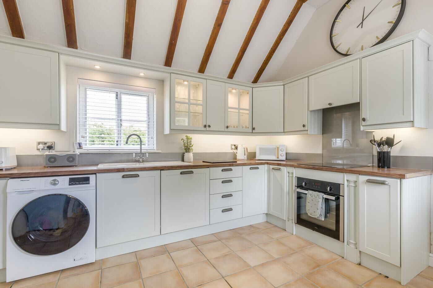 A modern kitchen with white cabinets, a built-in washing machine, a microwave, and a clock on the wall.