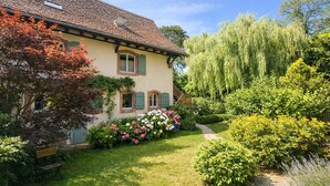 Une maison traditionnelle avec un toit en pente, une petite fenêtre avec des volets et un jardin bien entretenu, agrémenté de diverses plantes et fleurs.