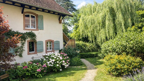 Une maison traditionnelle avec un chemin de jardin, un escalier en bois et une végétation luxuriante.