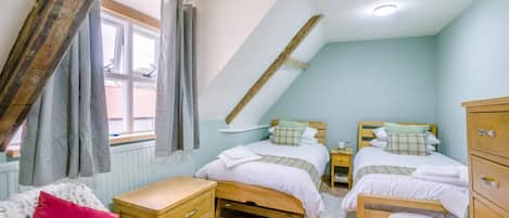 A bedroom with two beds, a wooden dresser, a small table, and a bench.