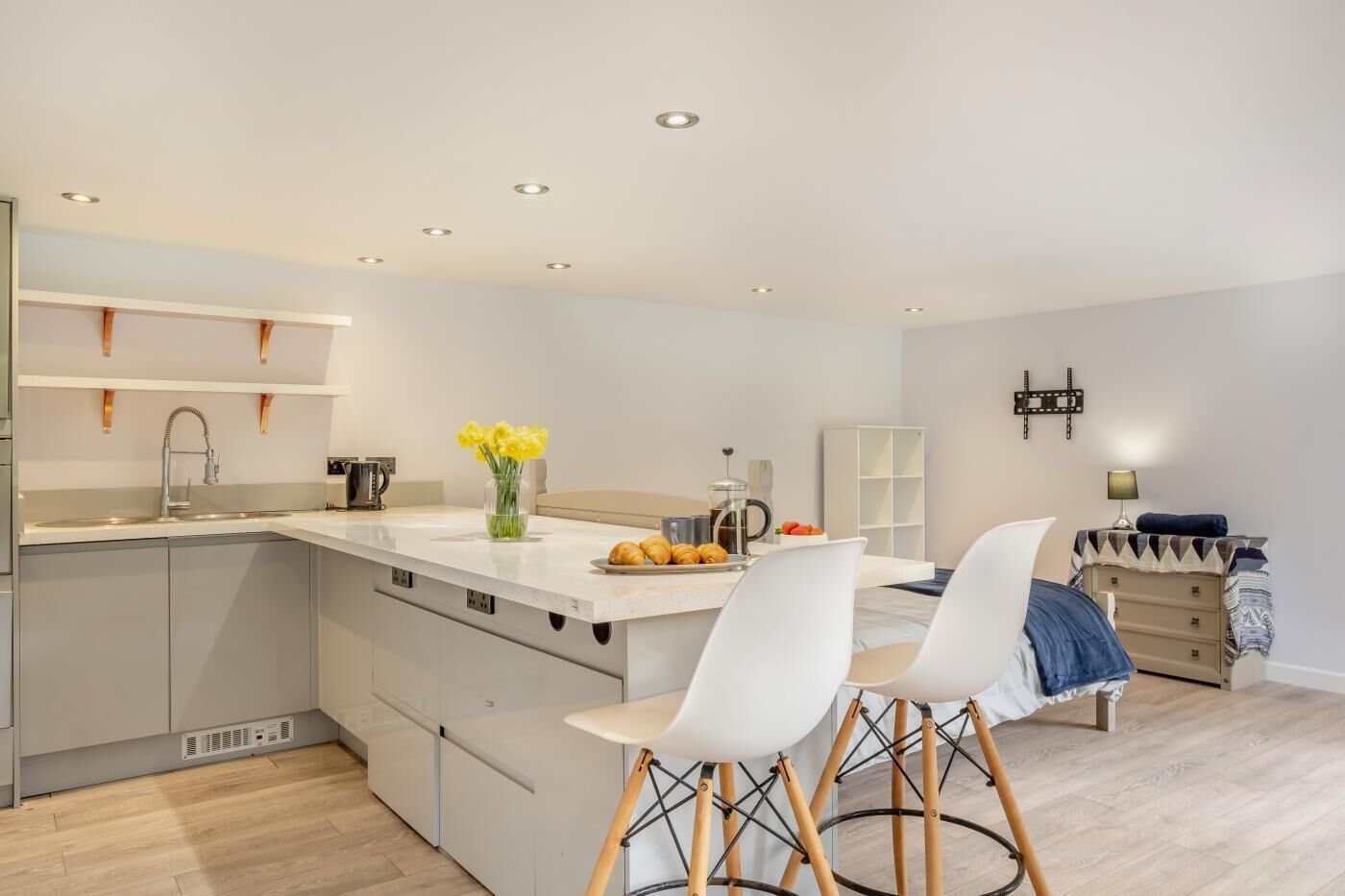 A modern kitchen with a central island, bar stools, a coffee machine, and a vase of flowers.