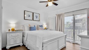 A bedroom with a bed, bedside tables, a ceiling fan, and a window with curtains. - Our House at the Beach C-113 (Siesta Key)