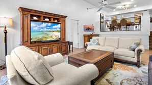 A living room with a television, sofa, armchair, coffee table, and a ceiling fan. - Our House at the Beach C-113 (Siesta Key)