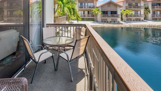A balcony with a table and chairs, overlooking a pool and a resort building. - Our House at the Beach C-113 (Siesta Key)